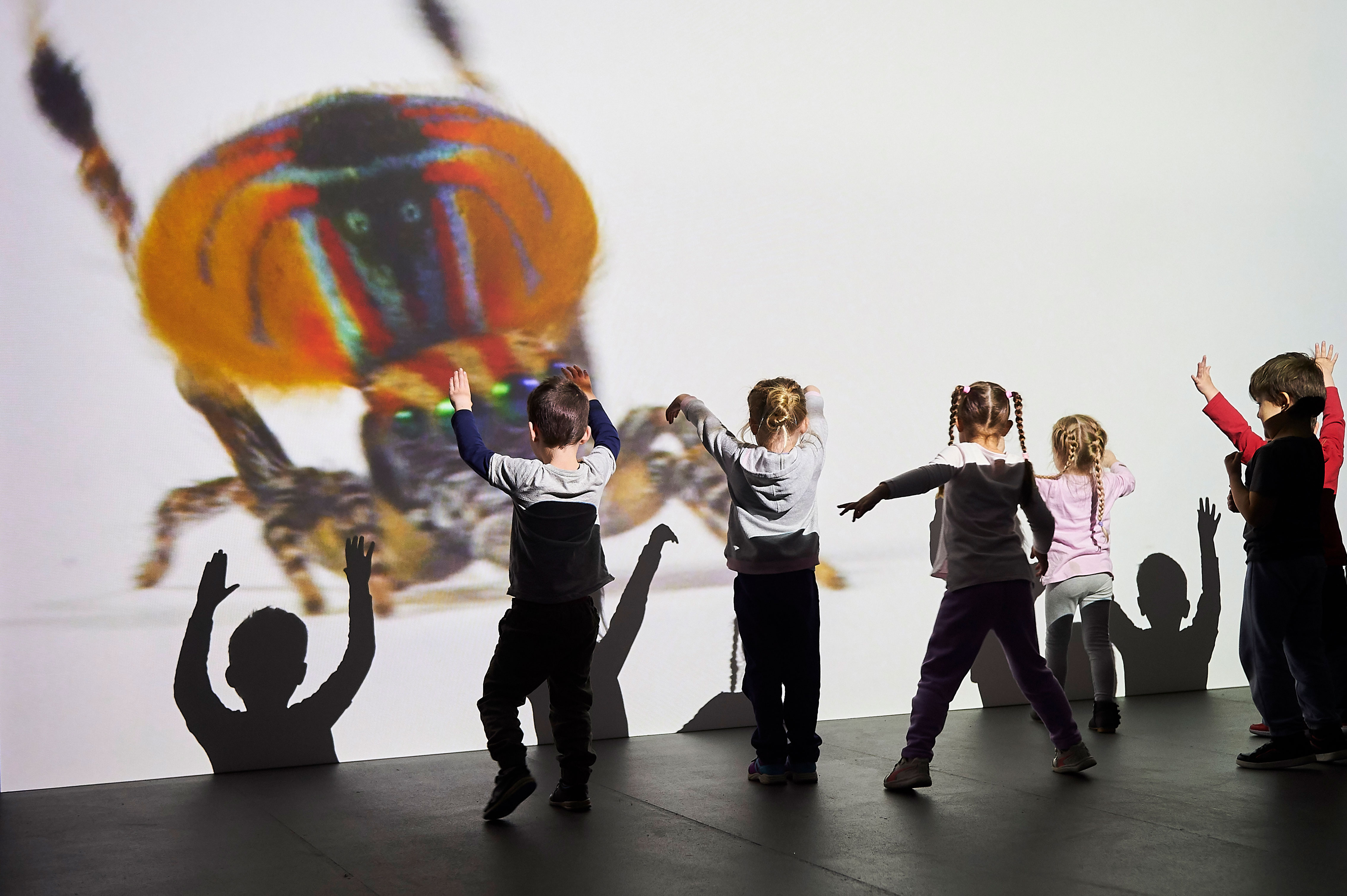 children dancing in front of a large projection of a spider