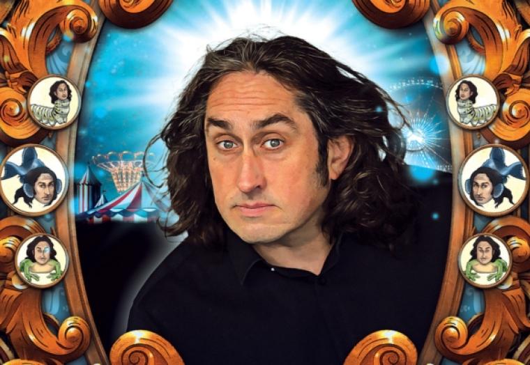 A man with long dark wavy hair looks through a frame that features buttons with his face on creatures - Ross Noble Cranium of Curiosities