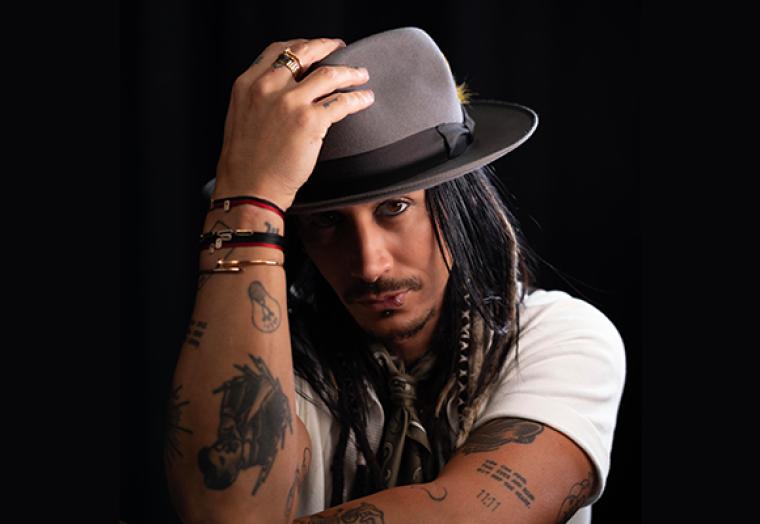 A man in a white t-shirt holds a hat on his head