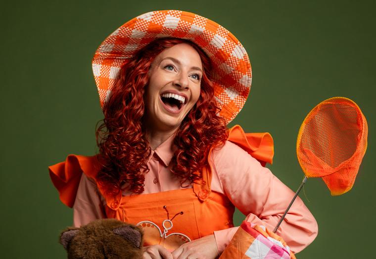 A woman with curly red hair wearing an orange dress smiles up at the camera