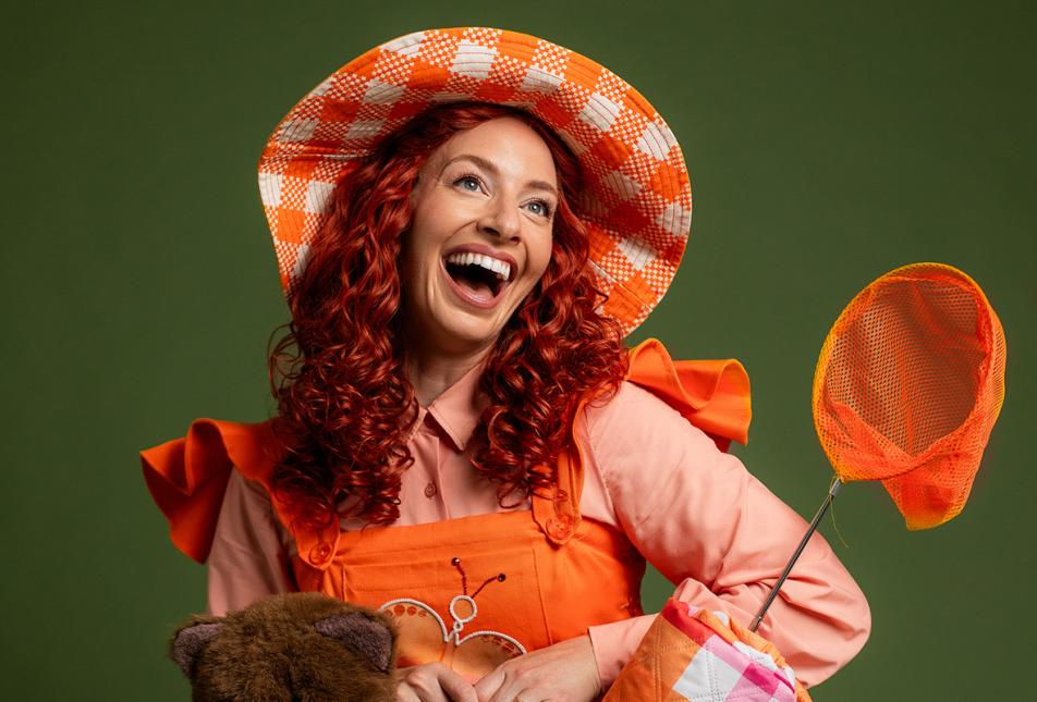 A woman with curly red hair wearing an orange dress smiles up at the camera