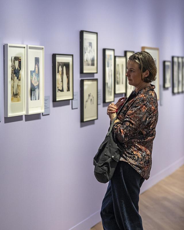 A woman looks at paintings on a purple wall 