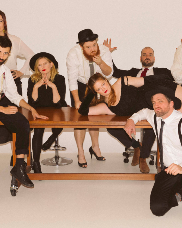 An eight-piece band sit around a table