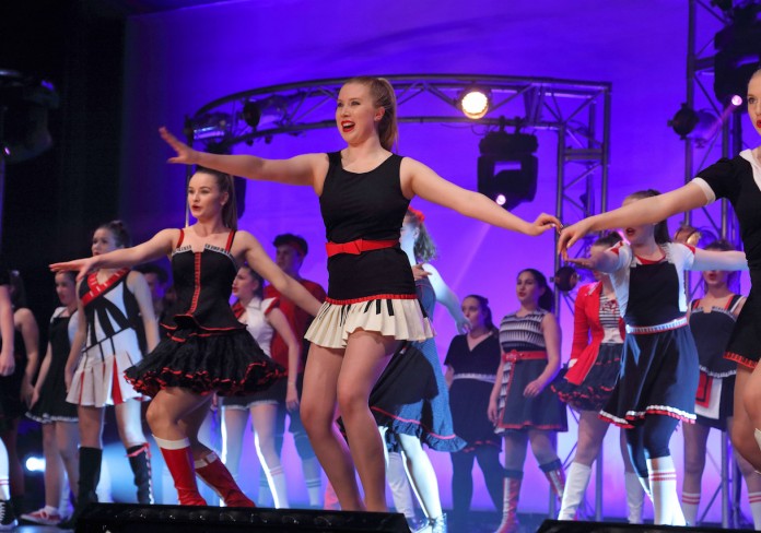 Young performers dancing on stage in costumes of red, black and white. 