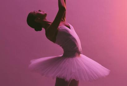 A ballet dancer in a tutu against a pink lit background