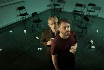 Two men stand in a room, looking up at a security camera