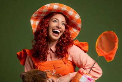 A woman with curly red hair wearing an orange dress smiles up at the camera